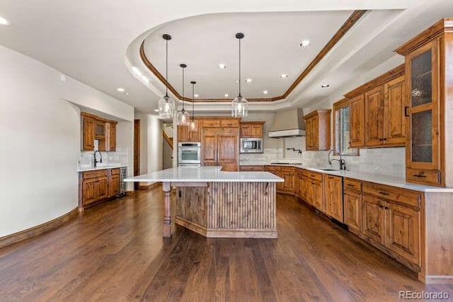 kitchen featuring a center island, a tray ceiling, pendant lighting, stainless steel appliances, and wall chimney range hood