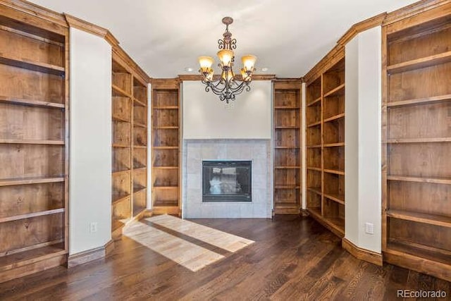 unfurnished living room with dark hardwood / wood-style floors, an inviting chandelier, a fireplace, and built in shelves