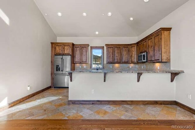 kitchen with a kitchen bar, lofted ceiling, appliances with stainless steel finishes, kitchen peninsula, and backsplash