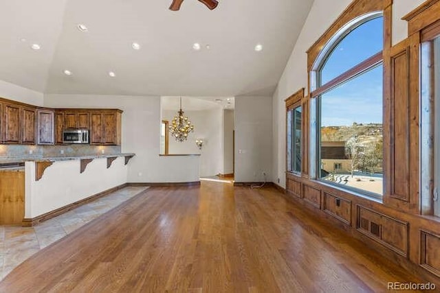 unfurnished living room with ceiling fan with notable chandelier, high vaulted ceiling, and light wood-type flooring