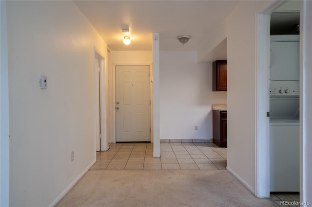 hallway featuring light colored carpet, baseboards, stacked washing maching and dryer, and light tile patterned flooring
