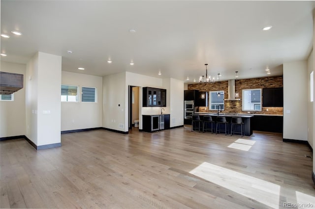 kitchen featuring a breakfast bar, tasteful backsplash, light wood-style floors, dark cabinets, and an inviting chandelier