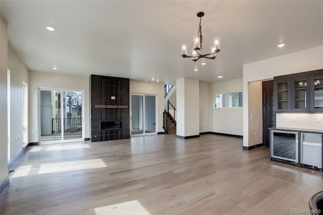 unfurnished living room with beverage cooler, stairway, a chandelier, and light wood-type flooring