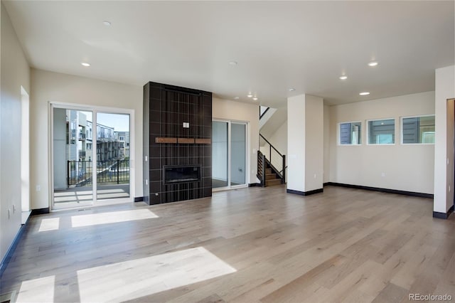 unfurnished living room featuring stairs, light wood-type flooring, and a fireplace