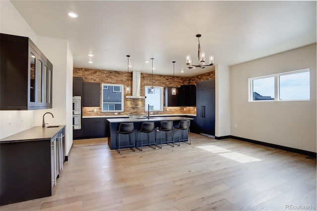 kitchen with wall chimney exhaust hood, a kitchen island, a breakfast bar area, backsplash, and a notable chandelier