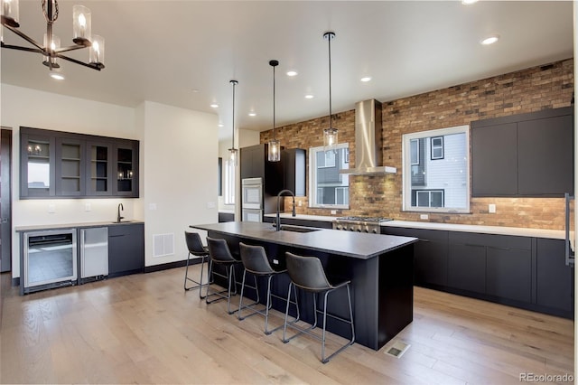 kitchen featuring visible vents, a center island with sink, a sink, a breakfast bar area, and wall chimney range hood