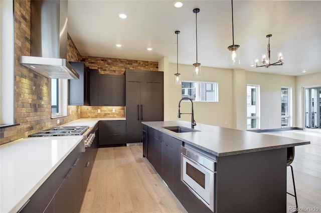 kitchen with modern cabinets, wall chimney exhaust hood, a sink, light wood-style floors, and an inviting chandelier