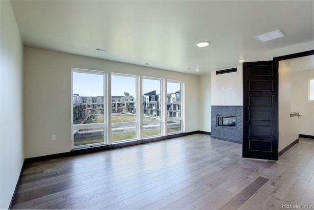 unfurnished living room featuring baseboards, visible vents, wood finished floors, and a glass covered fireplace