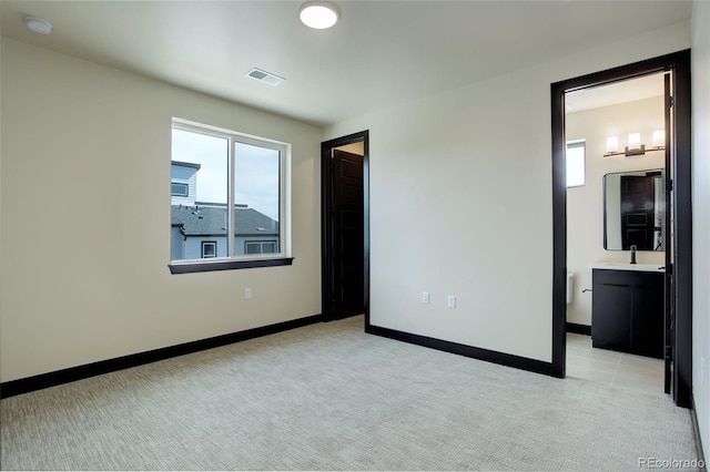 unfurnished bedroom with a sink, light carpet, baseboards, and visible vents