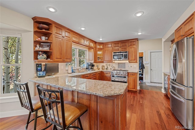 kitchen featuring light stone counters, stainless steel appliances, a kitchen breakfast bar, kitchen peninsula, and light hardwood / wood-style flooring