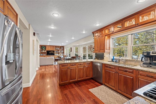 kitchen featuring sink, kitchen peninsula, light stone counters, appliances with stainless steel finishes, and dark hardwood / wood-style flooring