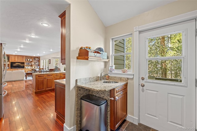 kitchen featuring wood-type flooring, kitchen peninsula, sink, stainless steel refrigerator, and light stone countertops