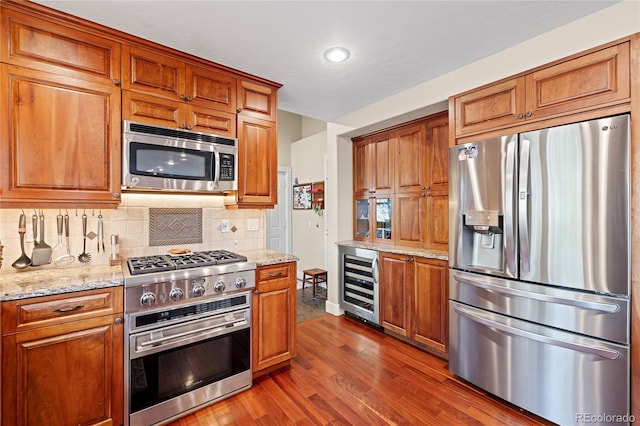 kitchen with stainless steel appliances, light stone counters, decorative backsplash, hardwood / wood-style flooring, and wine cooler