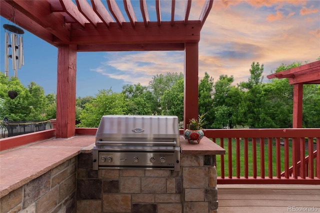 patio terrace at dusk with an outdoor kitchen, a deck, and grilling area