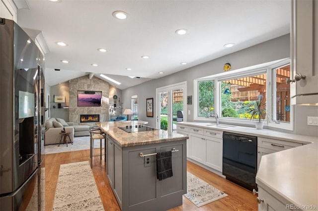 kitchen featuring black appliances, a fireplace, a center island, light wood-style flooring, and lofted ceiling