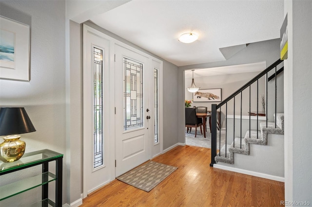 foyer entrance with wood finished floors, baseboards, and stairway