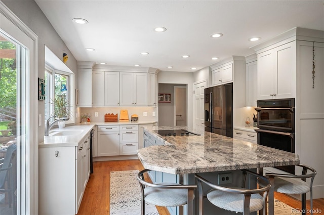 kitchen featuring black appliances, a sink, a center island, recessed lighting, and a kitchen bar