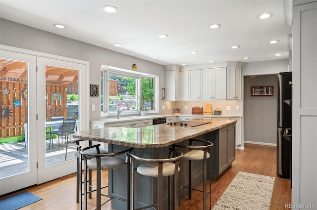kitchen featuring a kitchen island, light stone countertops, recessed lighting, a breakfast bar, and white cabinetry