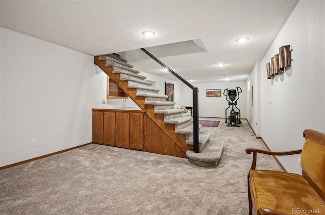 finished basement with a textured ceiling, stairway, light carpet, baseboards, and a sink