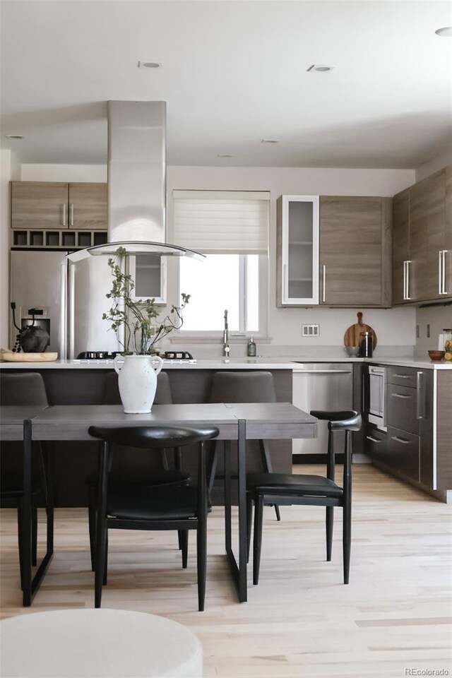 3615 Navajo St, Denver, CO 80211 - kitchen with appliances with stainless steel finishes, light countertops, light wood finished floors, and island exhaust hood