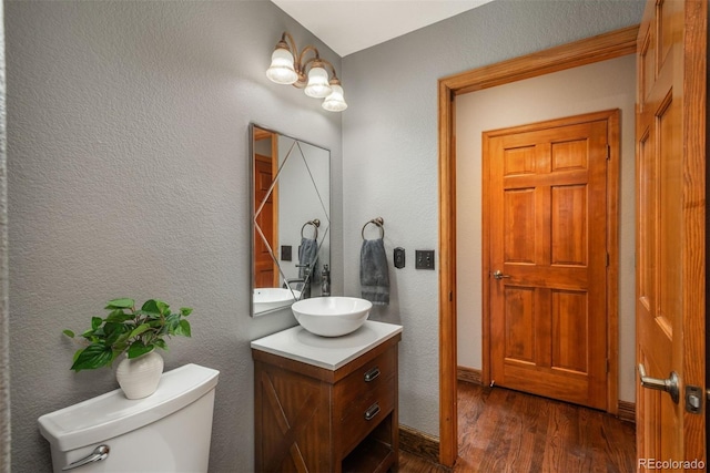 half bathroom featuring toilet, a textured wall, wood finished floors, and vanity