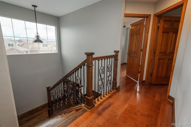 hallway featuring baseboards, wood finished floors, and an upstairs landing