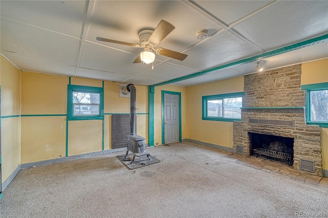 unfurnished living room featuring plenty of natural light, a fireplace, ceiling fan, and a wood stove