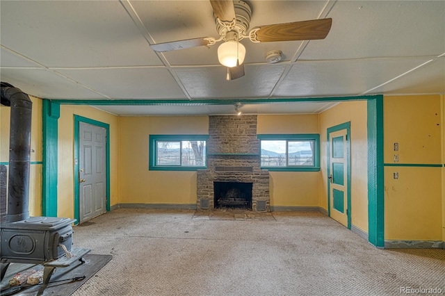 unfurnished living room featuring a wood stove, ceiling fan, and a fireplace