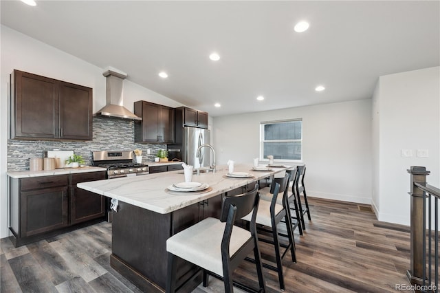260 Upper Glenway Rd, Palmer Lake, CO 80133 - kitchen featuring wall chimney range hood, a breakfast bar area, dark brown cabinetry, a kitchen island with sink, and tasteful backsplash