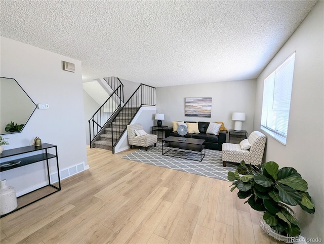 living room featuring stairway, baseboards, visible vents, light wood-style floors, and a textured ceiling