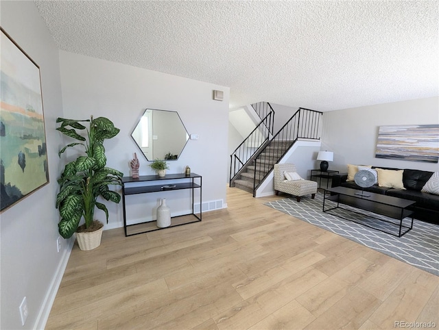 living area with stairway, wood finished floors, baseboards, visible vents, and a textured ceiling