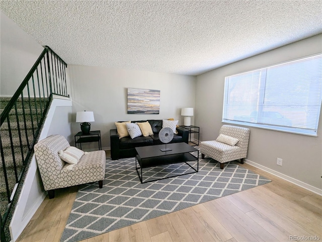 living area featuring baseboards, a textured ceiling, wood finished floors, and stairs