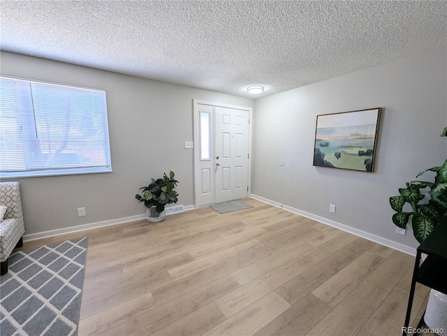 foyer featuring baseboards, light wood-style floors, and a textured ceiling