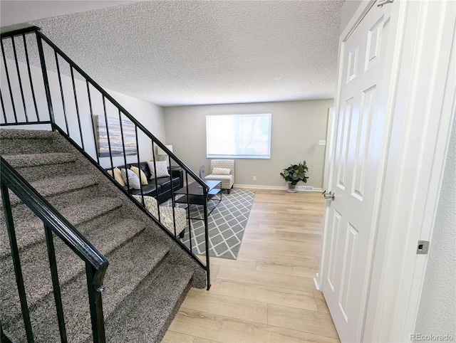 stairway featuring wood finished floors, baseboards, and a textured ceiling