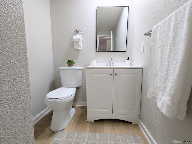 half bathroom with vanity, wood finished floors, baseboards, toilet, and a textured wall