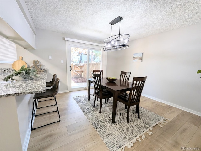 dining room with light wood-type flooring, baseboards, a textured ceiling, and a chandelier