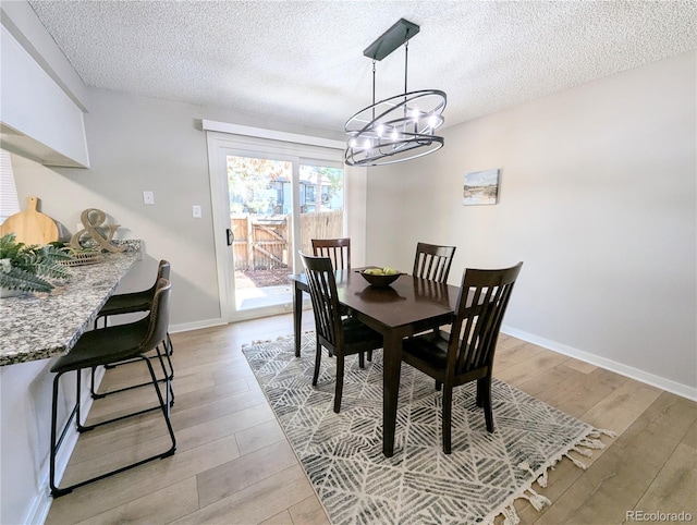 dining area featuring an inviting chandelier, a textured ceiling, light wood-type flooring, and baseboards