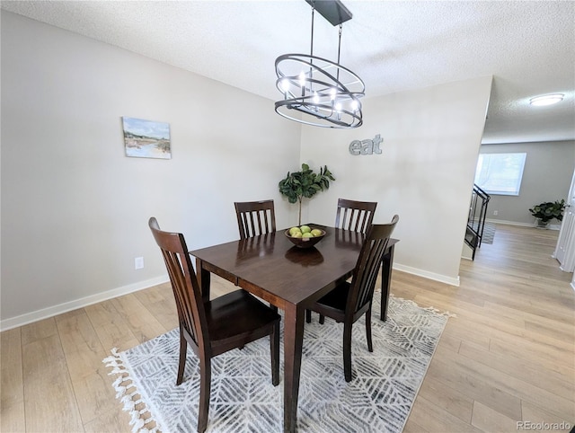 dining room with a notable chandelier, light wood-style floors, baseboards, and a textured ceiling