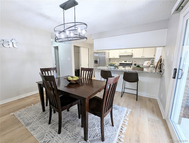 dining room with baseboards, a textured ceiling, a chandelier, and light wood finished floors