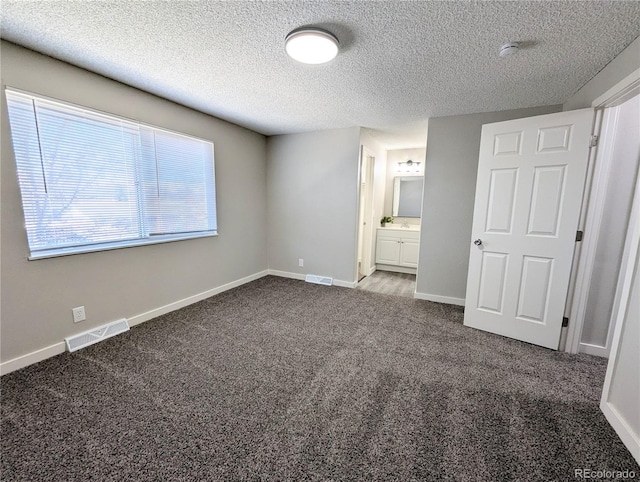 unfurnished bedroom featuring carpet, visible vents, baseboards, ensuite bath, and a textured ceiling