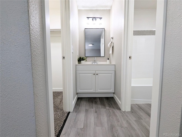 full bathroom with a textured wall, vanity, baseboards, and wood finished floors