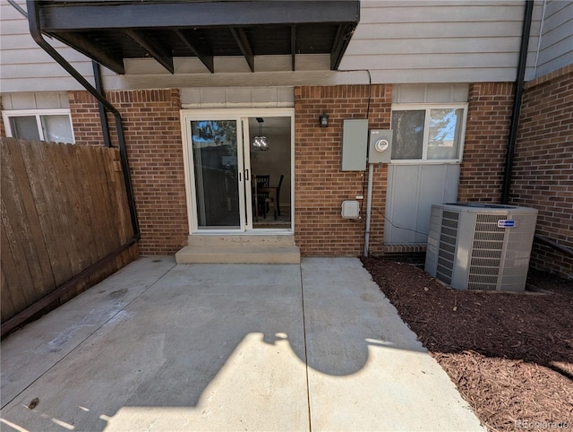 doorway to property with a patio area, fence, brick siding, and central AC