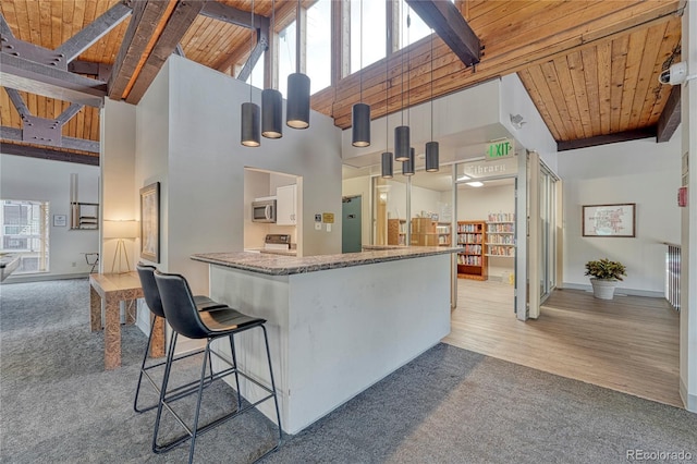 kitchen with beam ceiling, wooden ceiling, light colored carpet, and a towering ceiling