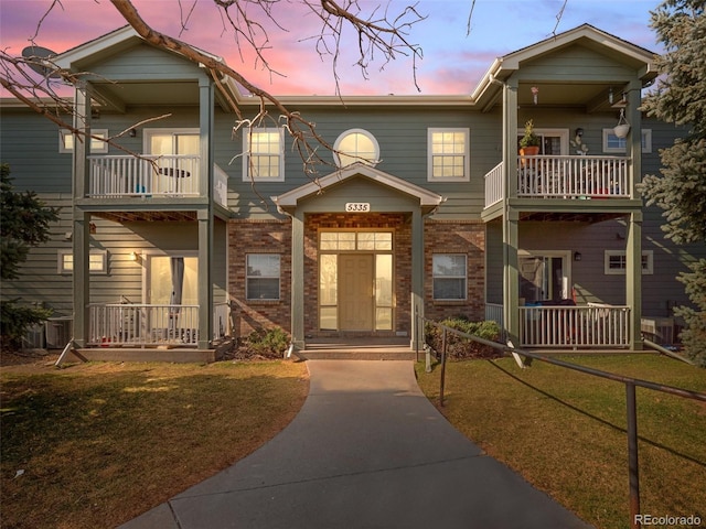 multi unit property featuring brick siding, a balcony, and a lawn