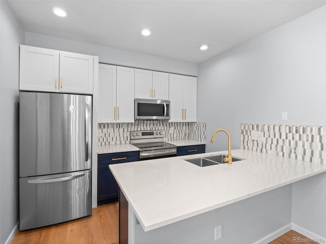 kitchen featuring backsplash, light stone countertops, appliances with stainless steel finishes, a peninsula, and a sink