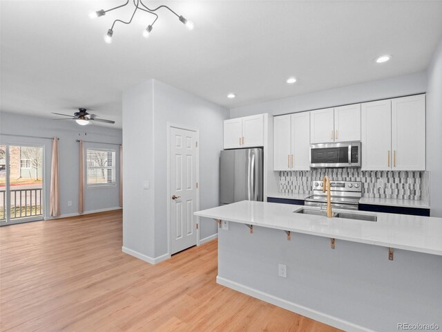 kitchen with a sink, a kitchen breakfast bar, backsplash, stainless steel appliances, and light countertops