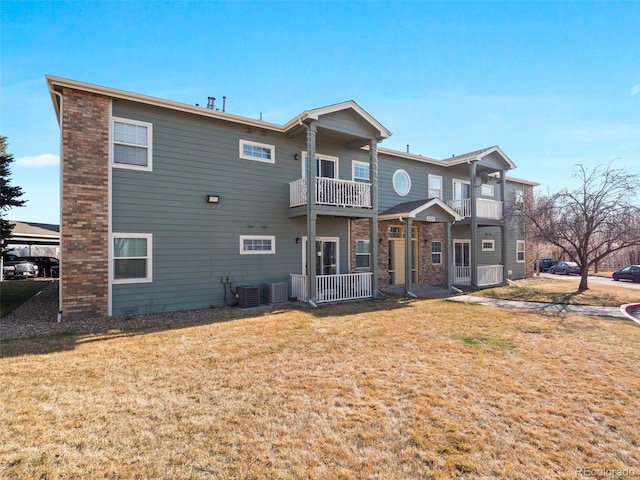 rear view of house featuring a yard, central air condition unit, a balcony, and brick siding