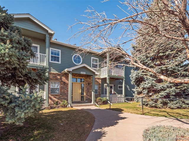 view of front of property with brick siding, a balcony, a front yard, and fence