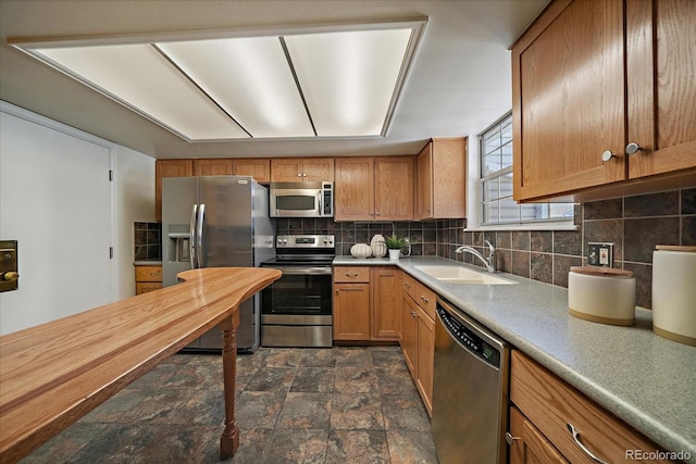 kitchen with stone finish flooring, light countertops, decorative backsplash, appliances with stainless steel finishes, and a sink