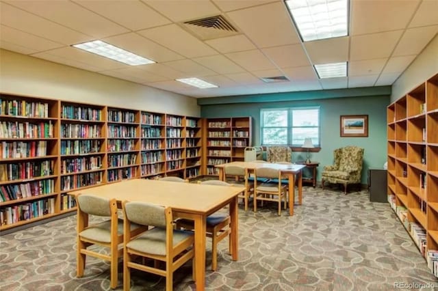 sitting room featuring bookshelves, visible vents, stone finish floor, and a paneled ceiling